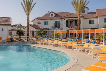 A pool with chairs and palm trees in front of a house at The Villas at Ellis Manor, Fresno, California